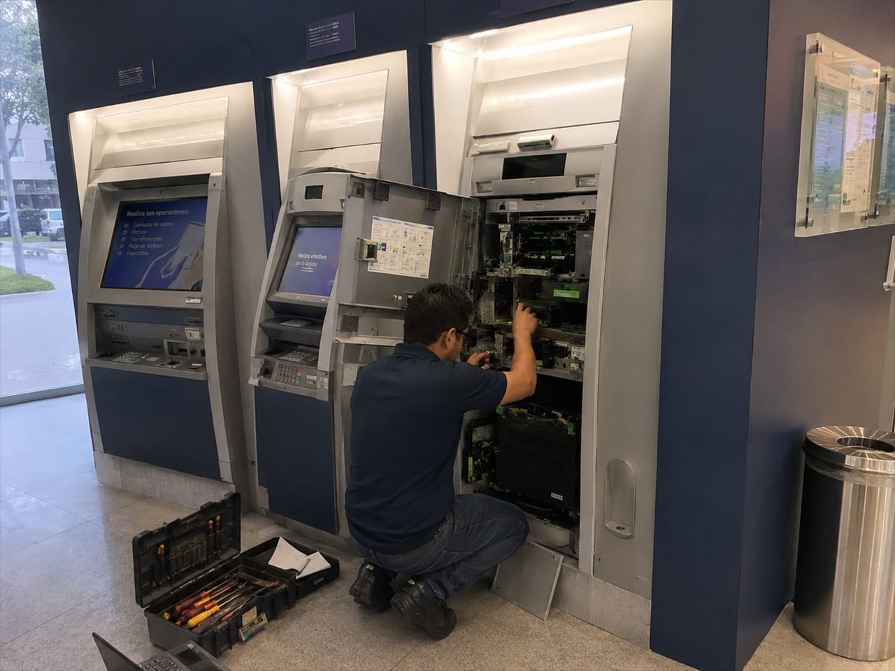 Técnico especializado realizando mantenimiento a un cajero automático sin logotipos bancarios visibles.